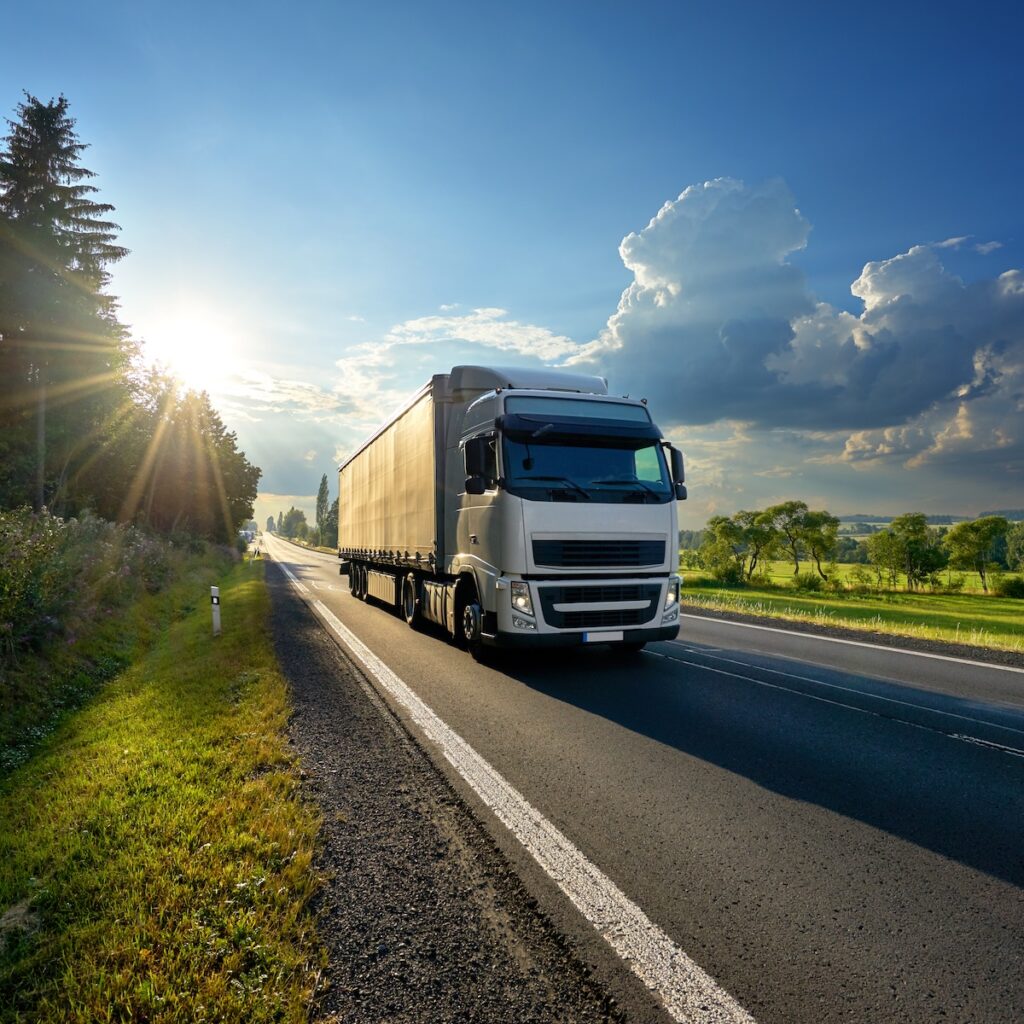 White truck arriving on the asphalt road in rural landscape in the rays of the sunset